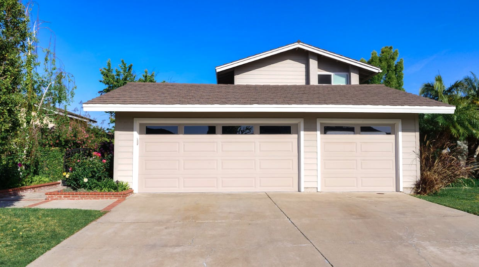 a pinkish beige colored house with a garage door and brown roof under the sun